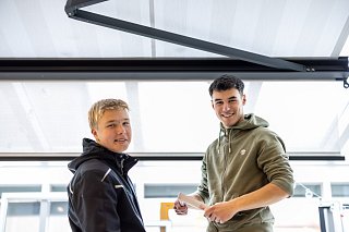 Zwei junge Mitarbeiter stehen unter einer Markise und lächeln in Kamera