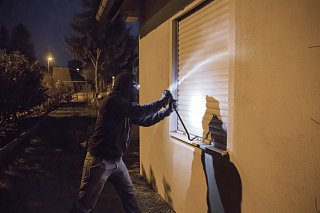 Einbrecher versucht bei Nacht Fenster mit Rollläden aufzubrechen