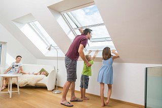 Familie steht an geöffnetem Dachflächenfenster, welches mit Insektenschutz ausgestattet ist