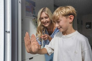 Mutter und Sohn berühren das feine Gewebe eines Insektenschutzes von Erfal