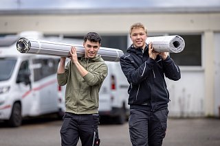 Zwei junge Mitarbeiter tragen Rollläden auf den Schultern