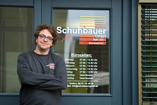Georg Schuhbauer vor dem Büro mit aufgedruckten Öffnungszeiten auf der Tür